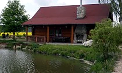 Roubený srub u rybníka s červenou střechou